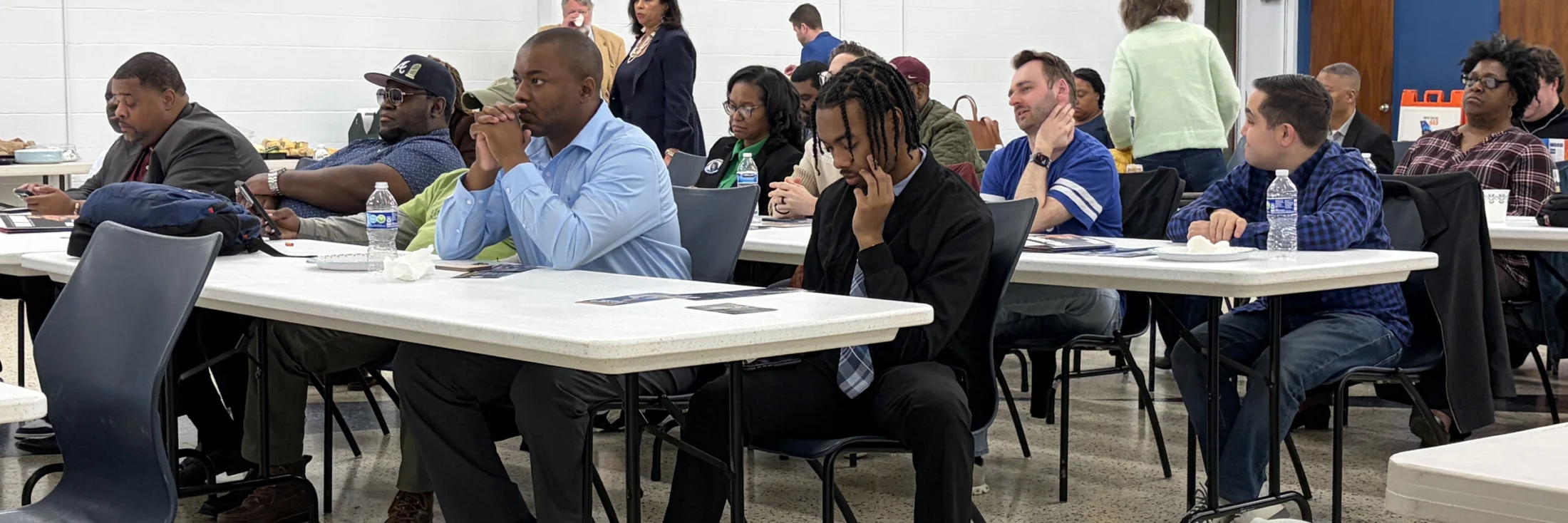 Committee members seated at long tables during a monthly meeting, several taking notes.